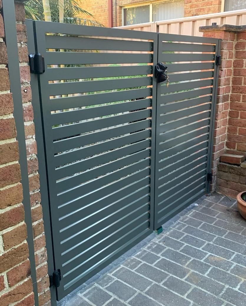 A Metal Gate Is Sitting Next to A Brick Wall — Optimum Aluminium Fabrication in Barrack Heights, NSW