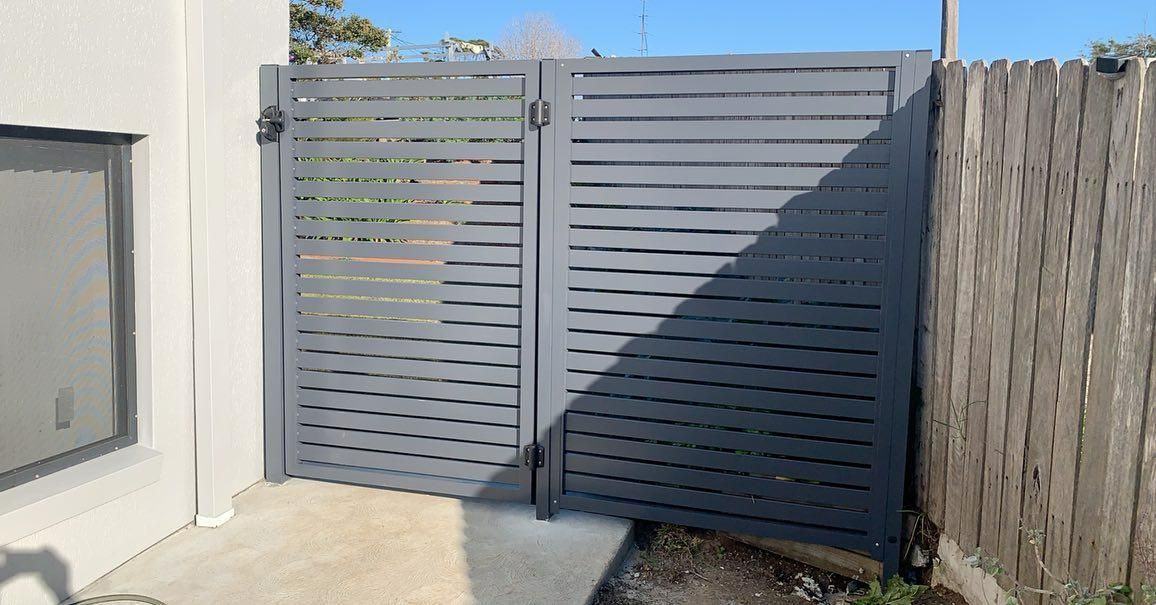 A Gray Gate Is Sitting Next to A Wooden Fence — Optimum Aluminium Fabrication in Barrack Heights, NSW