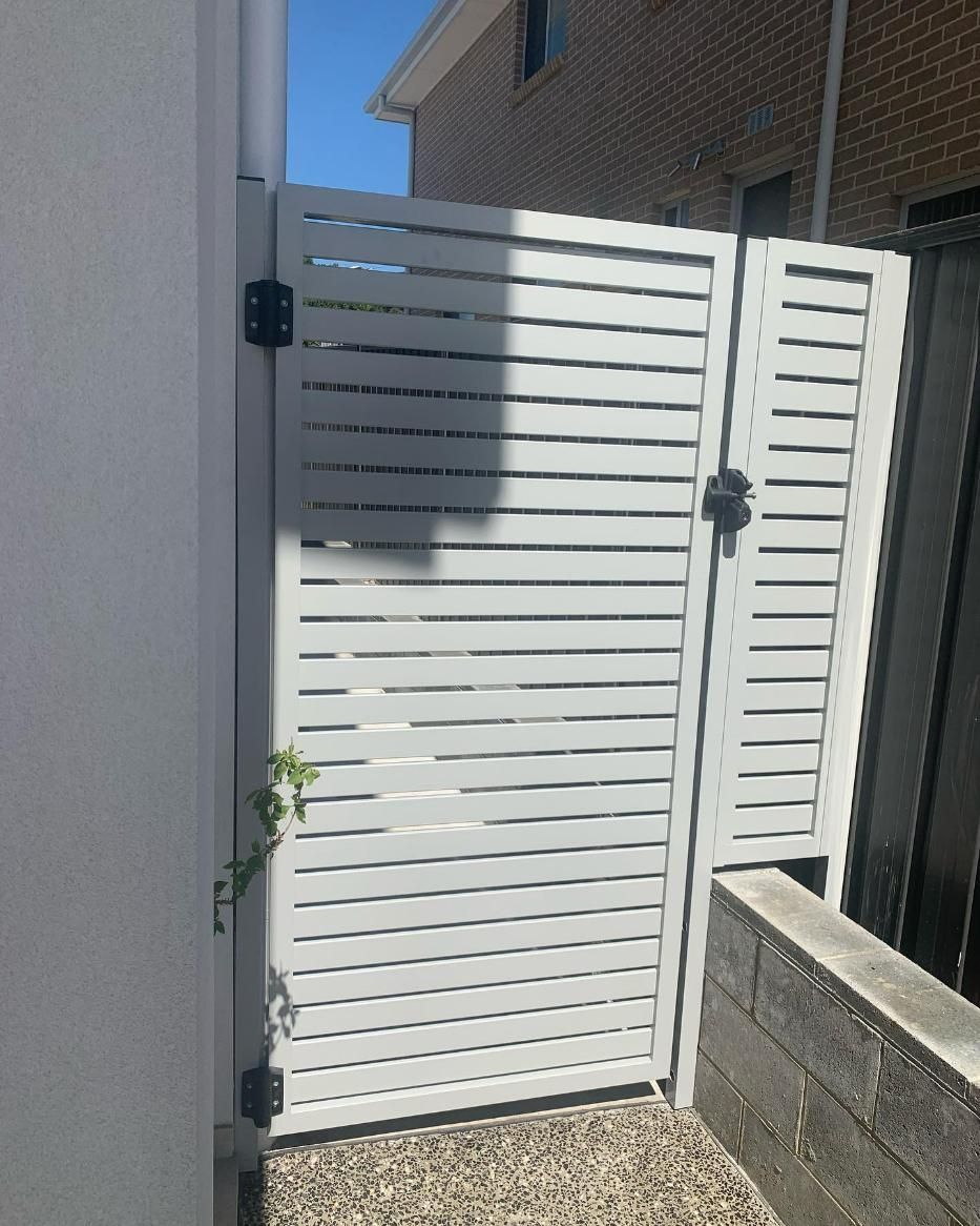A White Gate Is Sitting Next to A Brick Wall — Optimum Aluminium Fabrication in Barrack Heights, NSW
