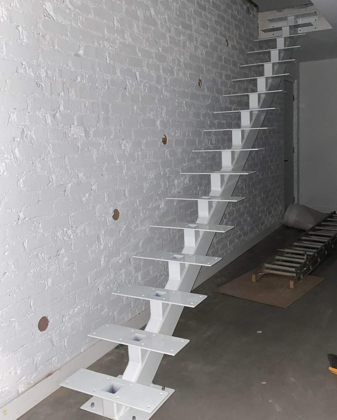A White Staircase Is Being Built in Front of A White Brick Wall — Optimum Aluminium Fabrication in Barrack Heights, NSW