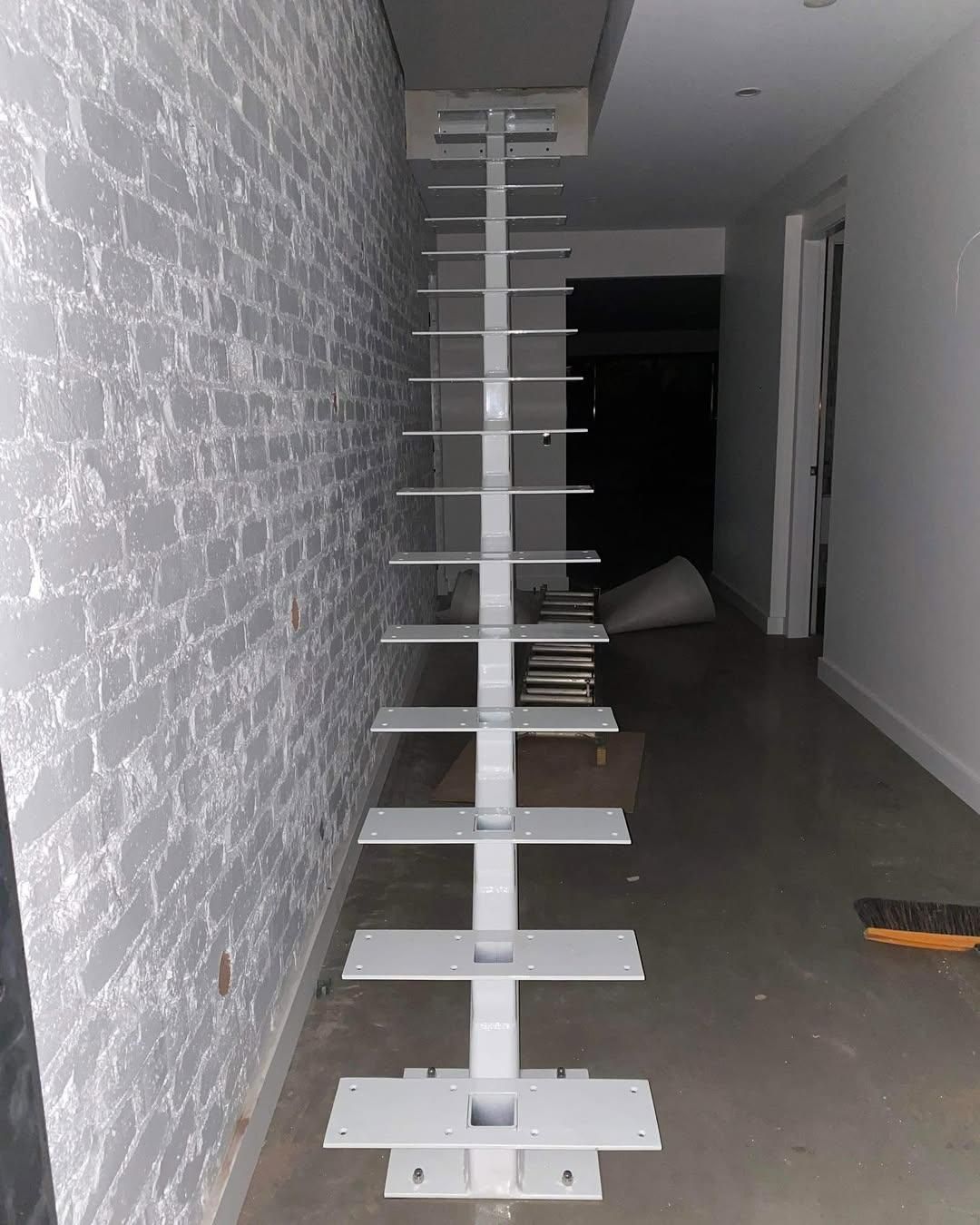 A White Staircase Is Sitting in A Hallway Next to A Brick Wall — Optimum Aluminium Fabrication in Barrack Heights, NSW