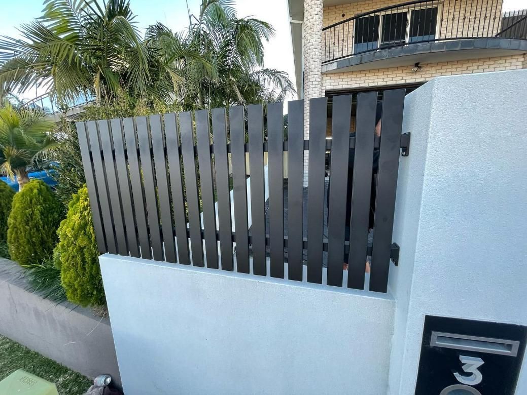 A Wooden Fence Is Sitting on Top of A White Wall Next to A House — Optimum Aluminium Fabrication in Barrack Heights, NSW
