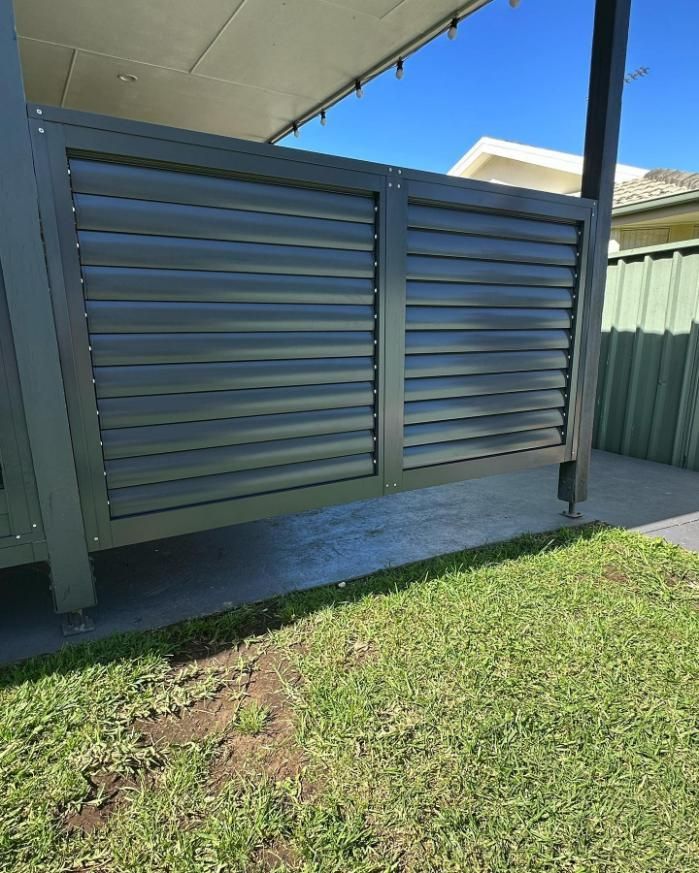 A Fence with Shutters on It Is in The Grass in Front of A House — Optimum Aluminium Fabrication in Barrack Heights, NSW