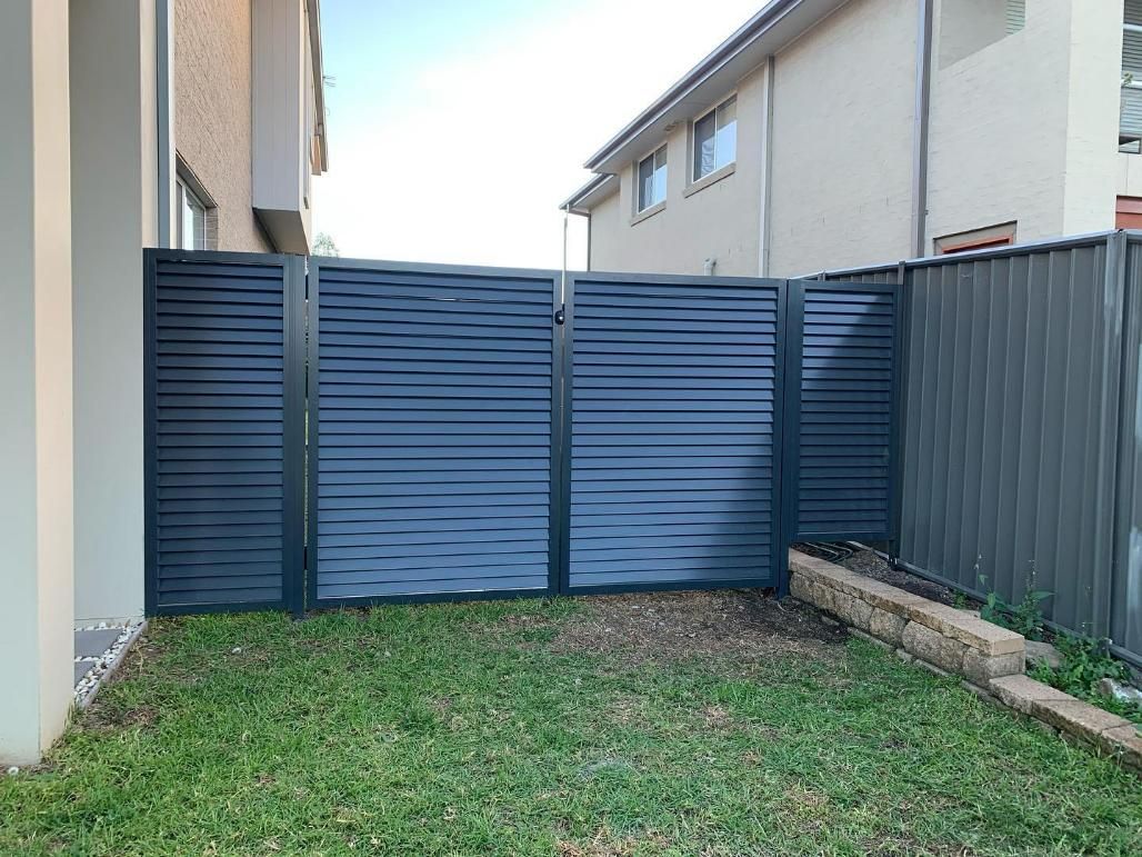 A Black Fence Surrounds a Lush Green Yard in Front of A House — Optimum Aluminium Fabrication in Albion Park, NSW