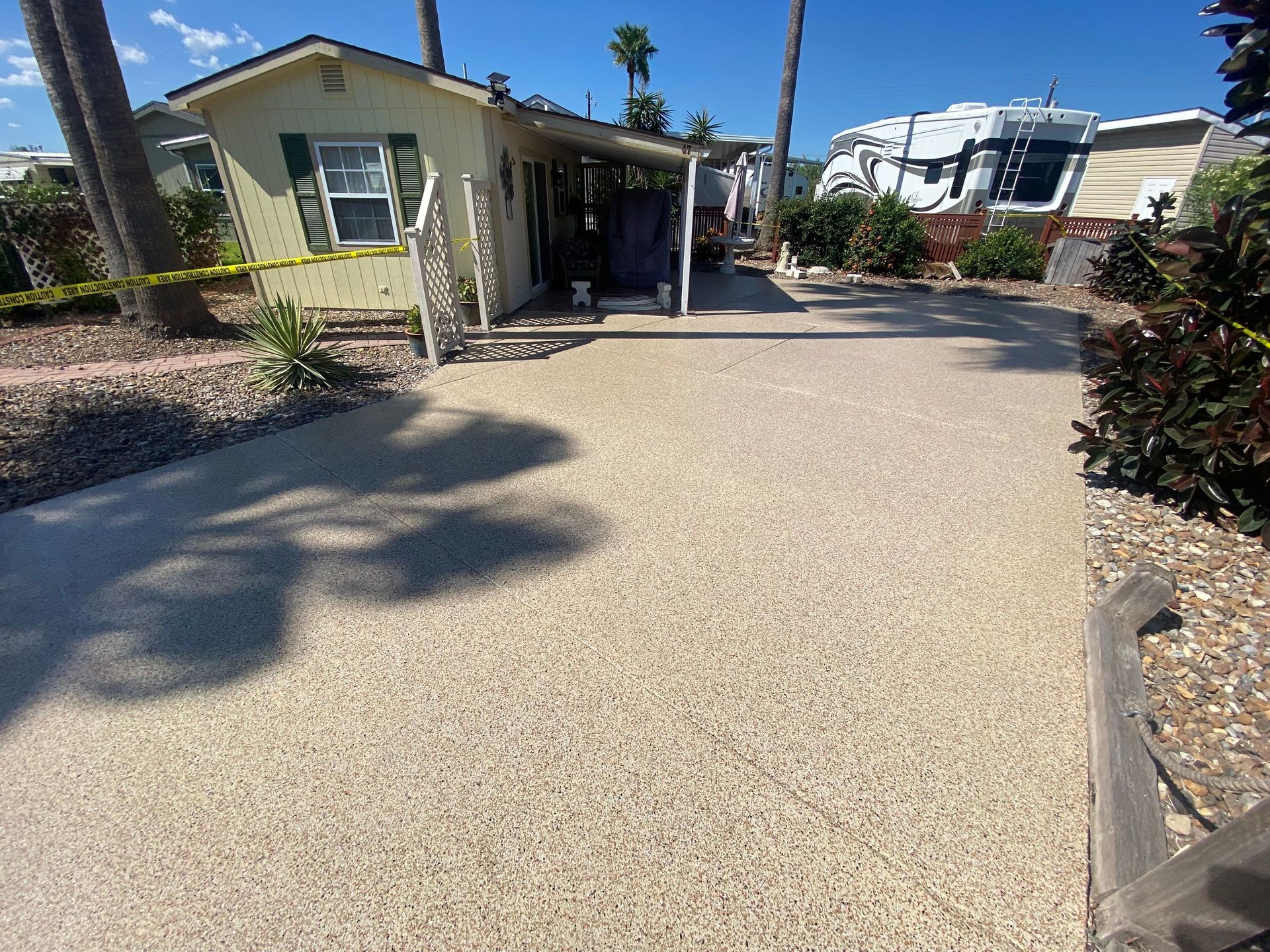 A gravel driveway leads to a light green bungalow, with a palm tree on either side.