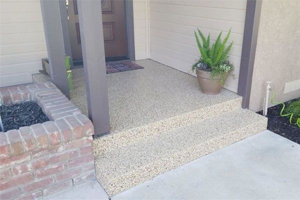 Entryway with beige aggregate steps, a potted plant, and a brick planter.