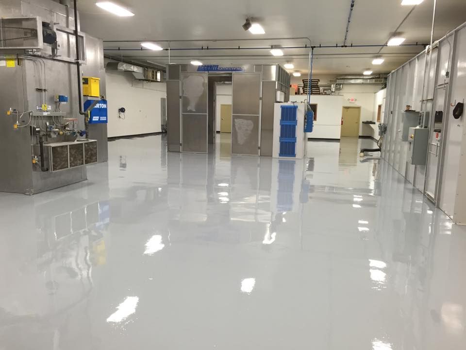 Shiny, light-gray floor in a clean, industrial space with stainless steel equipment and white walls.