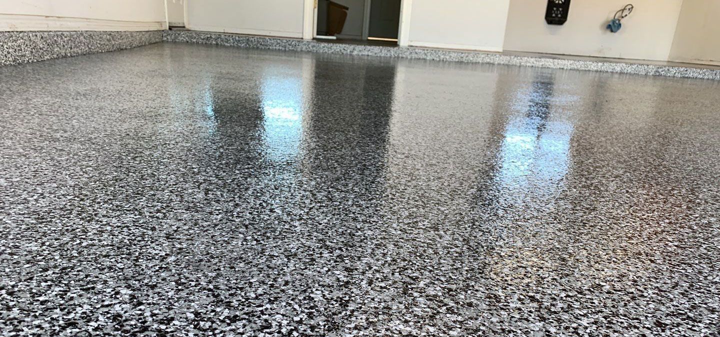 A glossy, speckled garage floor. The floor appears to be coated in epoxy, reflecting natural light.