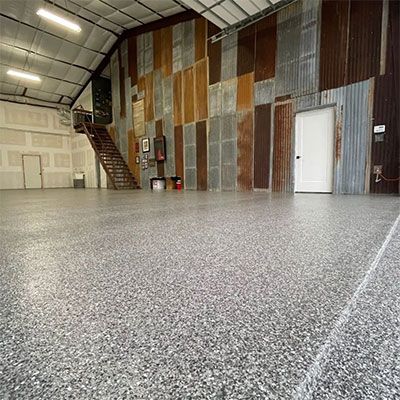 Large industrial space with epoxy floor, metal walls, and staircase.