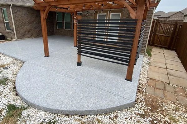 Concrete patio with pergola, black screen, brick house, and stone pathway.