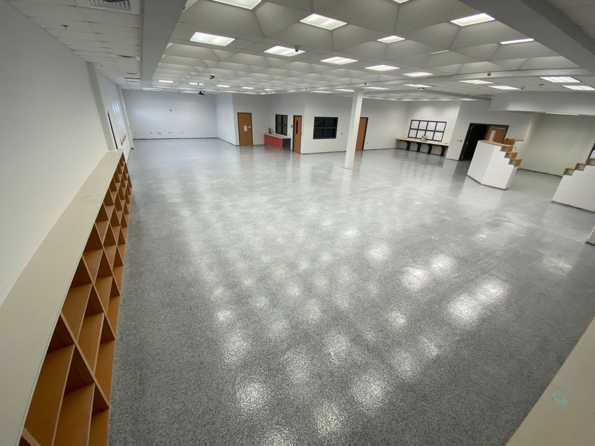 Large empty room with a shiny speckled floor, bright overhead lights, and built-in shelving on one side.