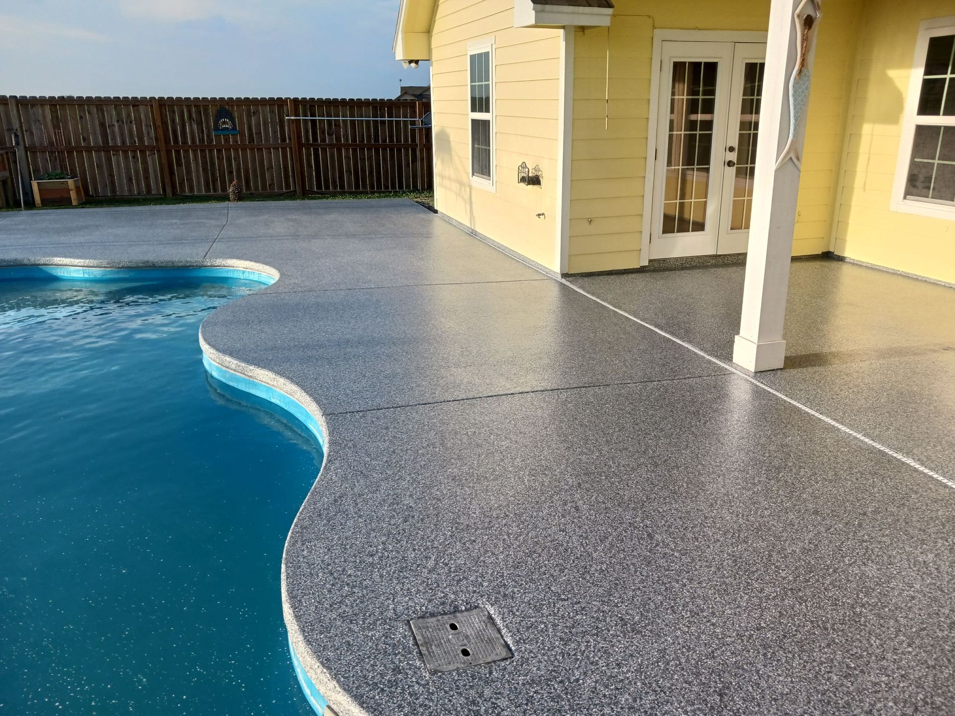 Poolside with gray speckled concrete and a yellow house.