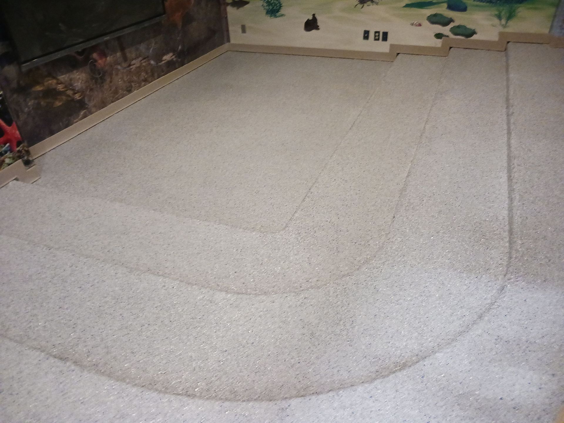 Indoor model race track with curved corners; light gray surface, wooden borders, and tan wall.