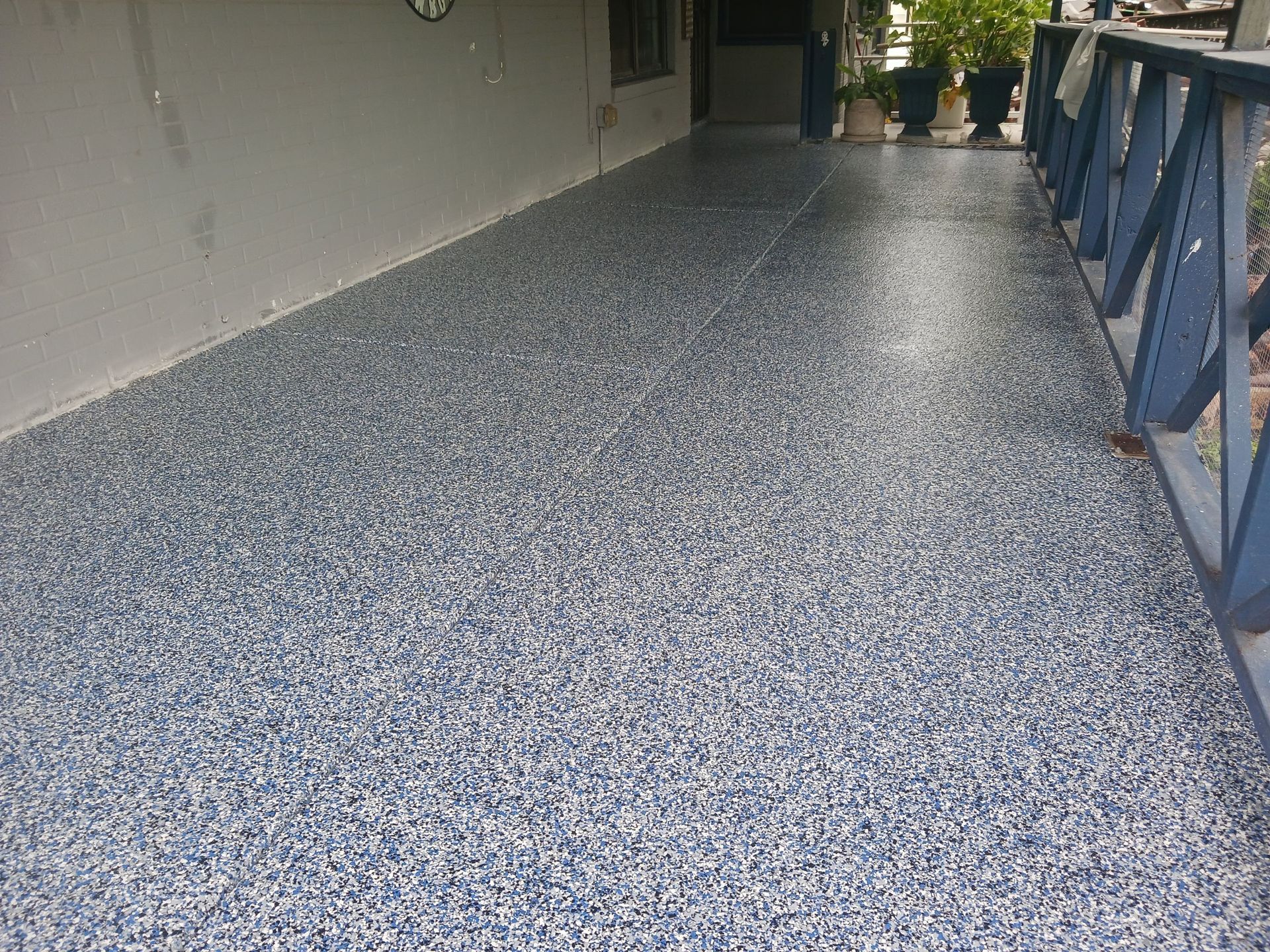 Porch floor with blue, white, and gray flecks, next to a blue railing.