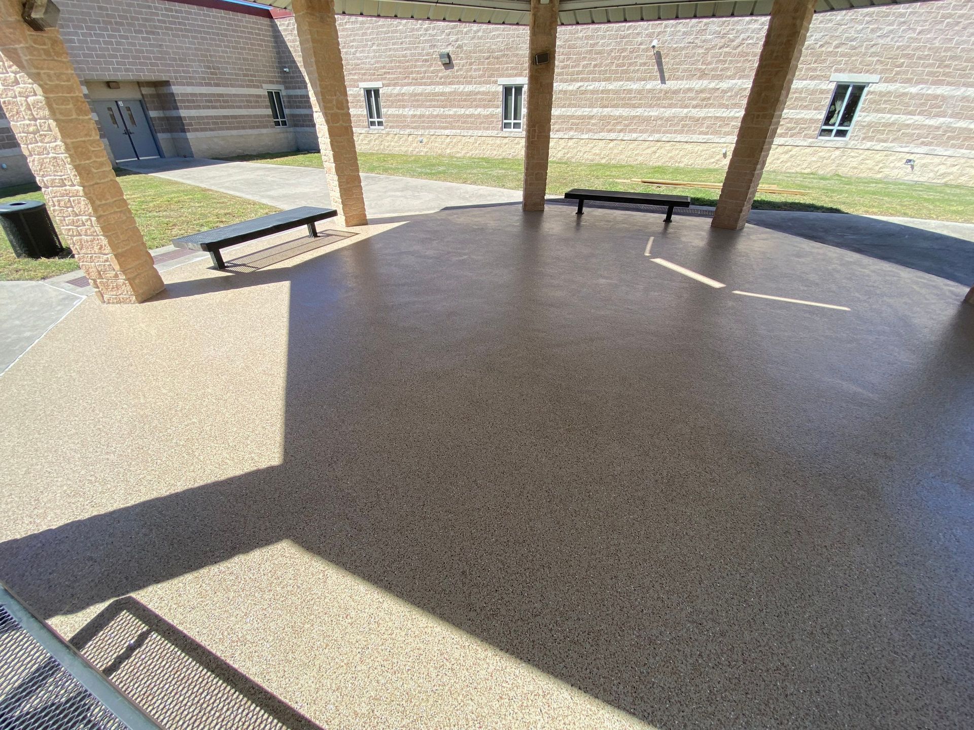 Covered concrete patio with benches, brown brick building in the background.