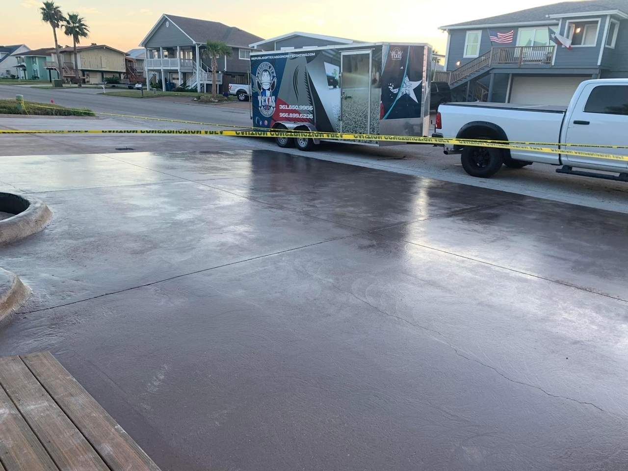 Wet, freshly poured concrete driveway; a trailer and truck are parked nearby.