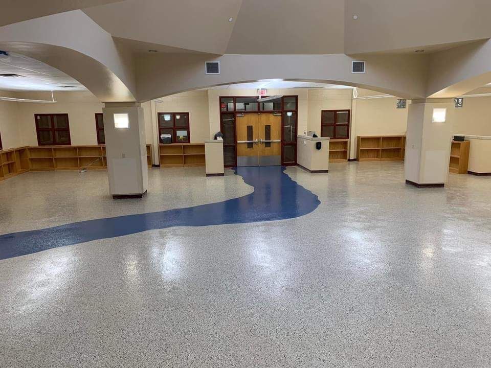 Empty school hallway with a blue and white speckled floor, wood bookshelves, and a double door.