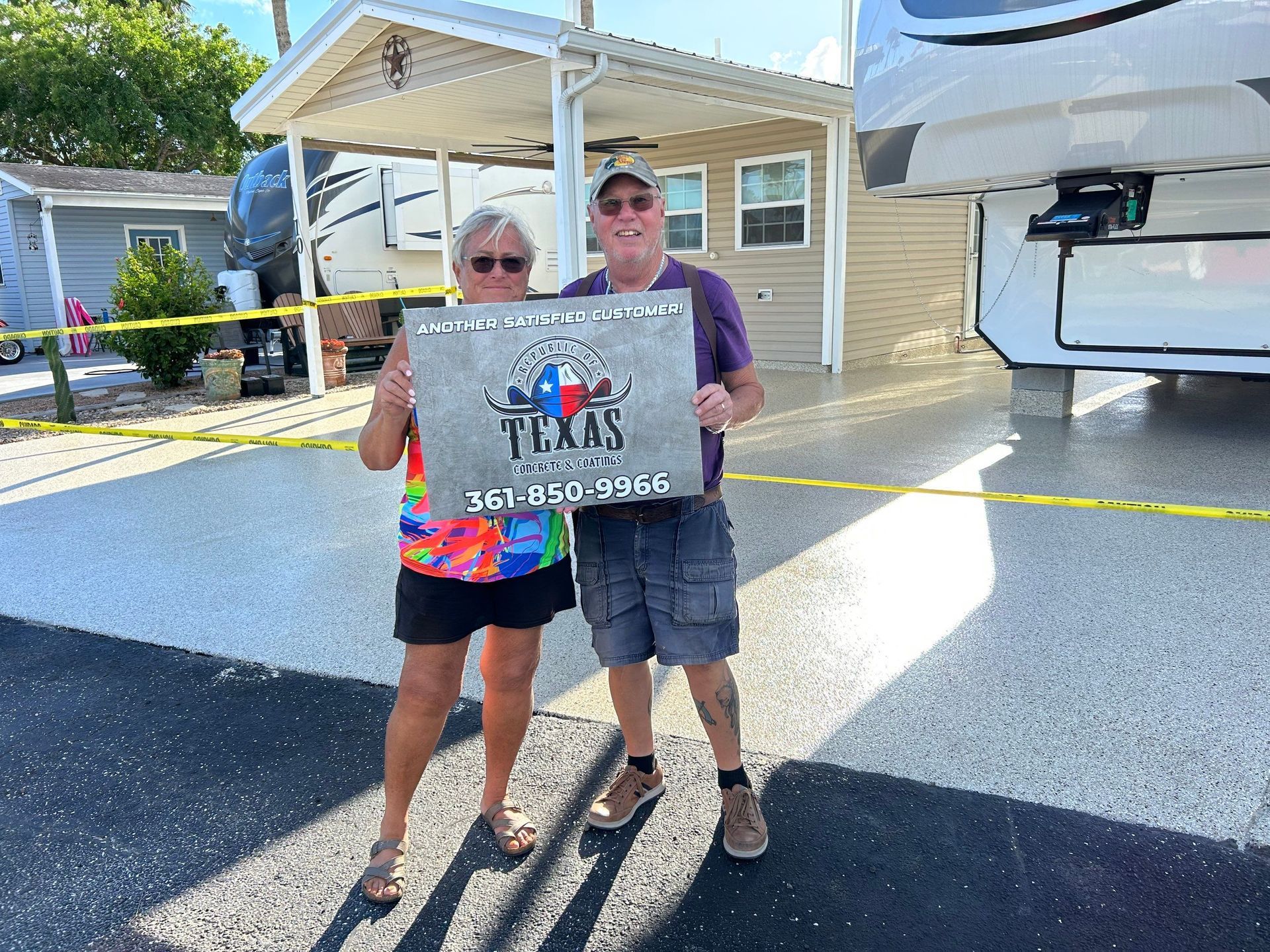 Two people holding a Texas-themed sign in front of RVs and a small building.