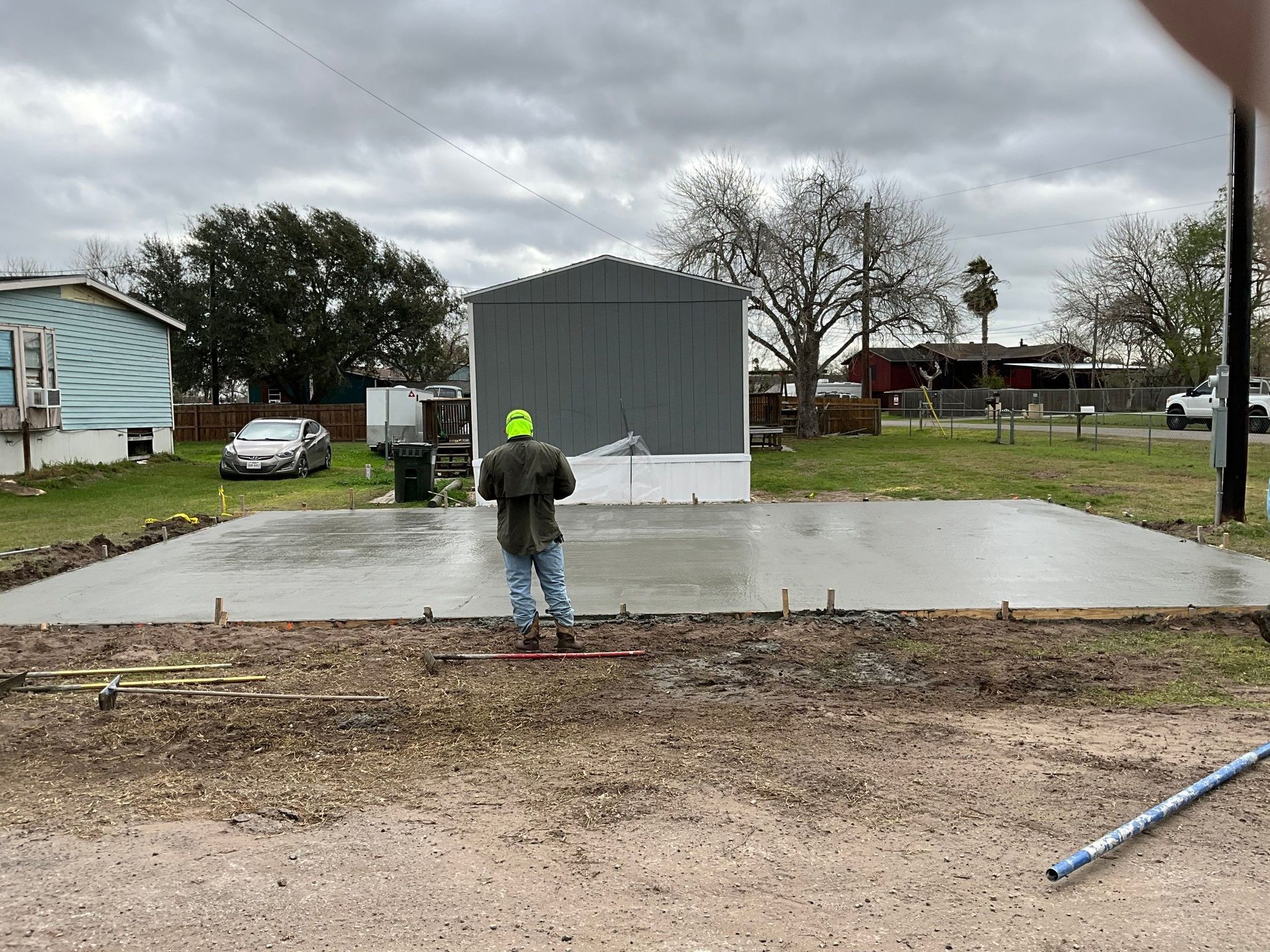 Man smoothing wet concrete slab in front of a gray metal building on an overcast day.