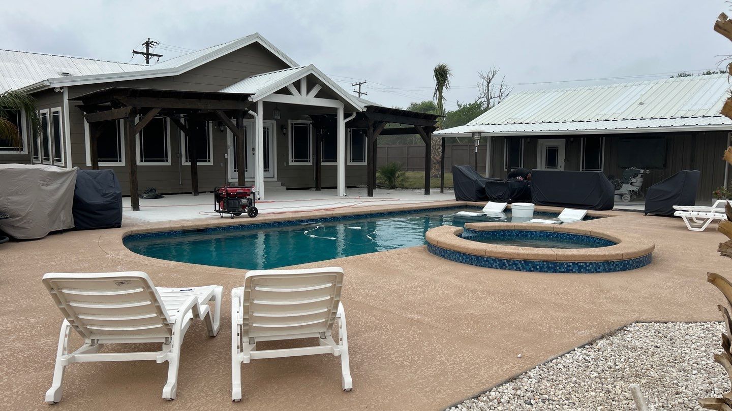 Backyard with pool, jacuzzi, lounge chairs, covered patio, and gray house.