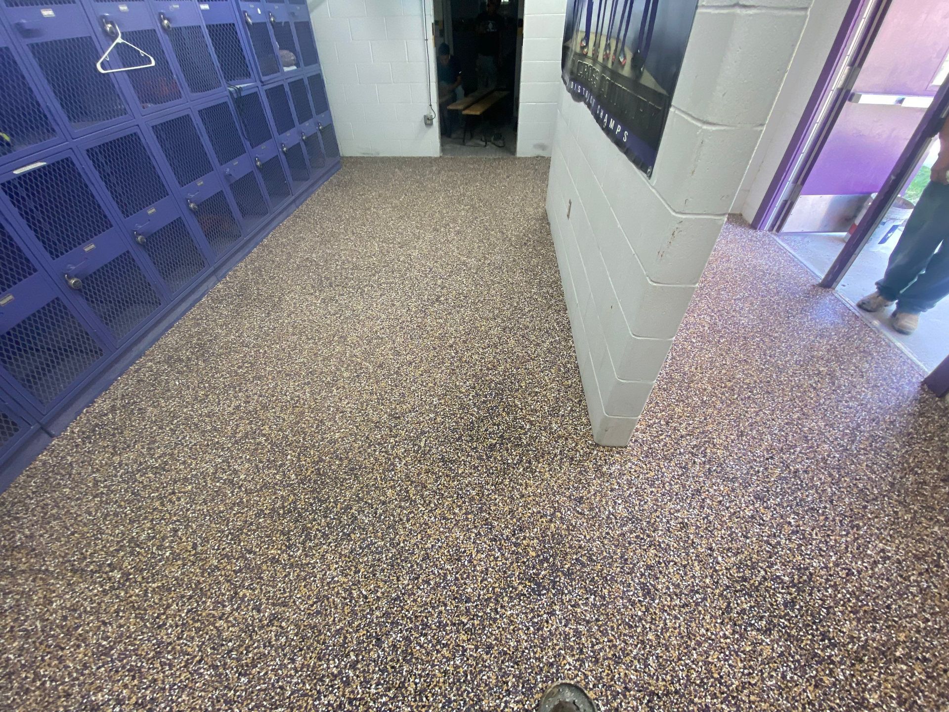 Locker room with purple lockers, speckled flooring, a doorway, and a person standing in a doorway.