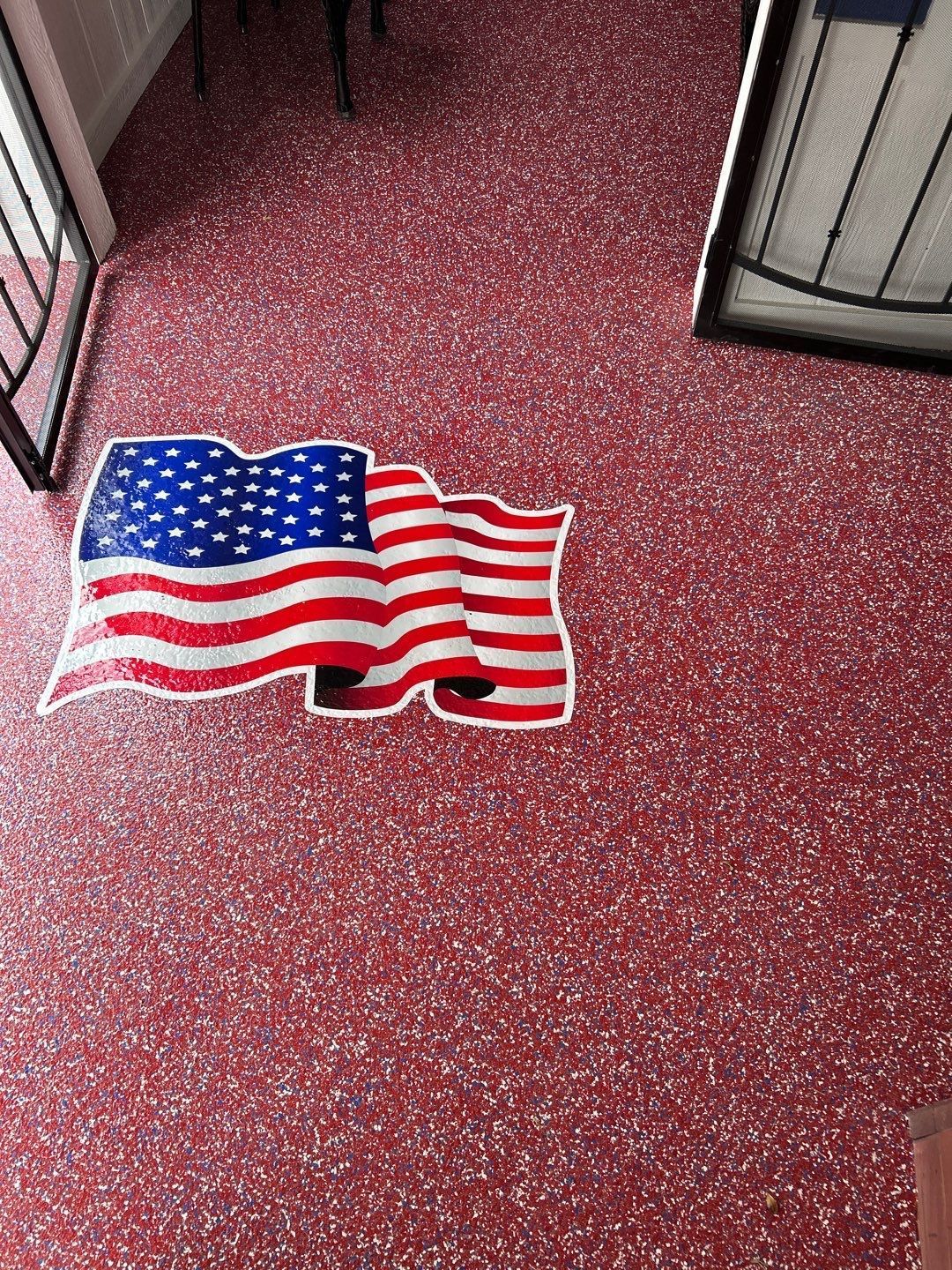 American flag on a textured red floor, near a black door and railing.