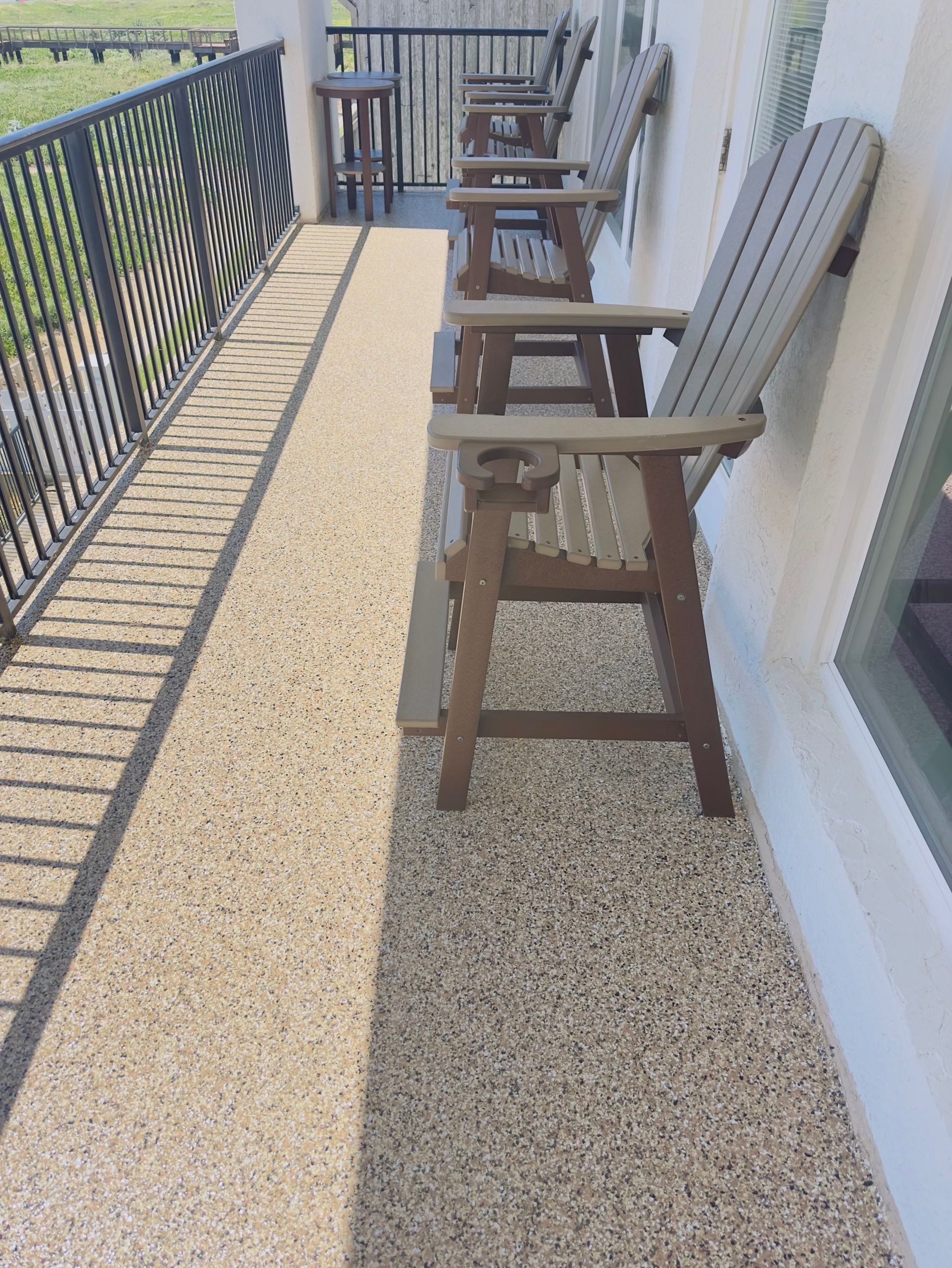 A narrow outdoor balcony with bar stools and a decorative railing casting a long shadow.