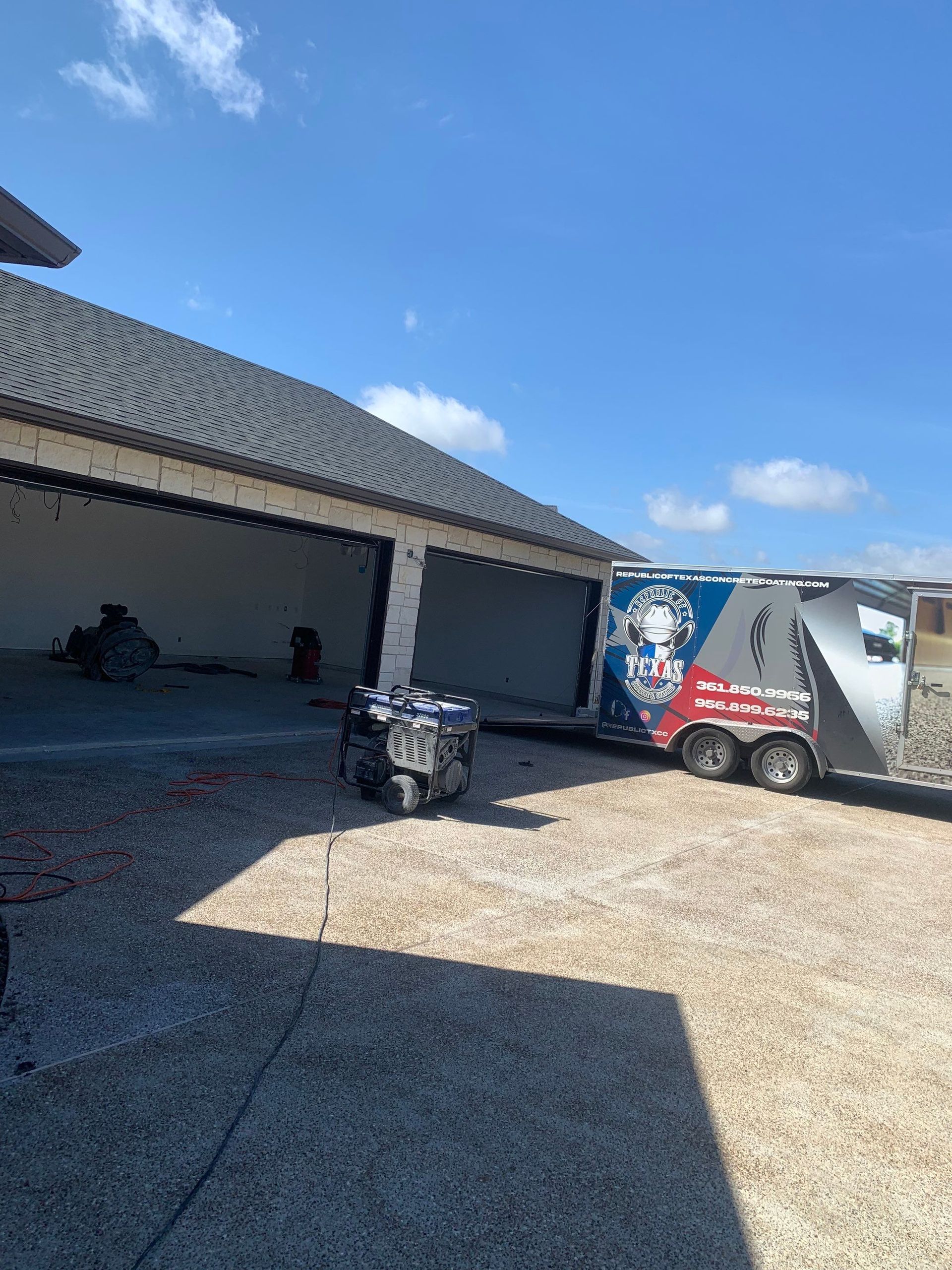 Garage with open doors, trailer parked outside, blue sky.