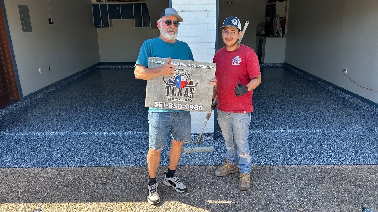 Two men in garage holding a sign, a gray and blue speckled floor.