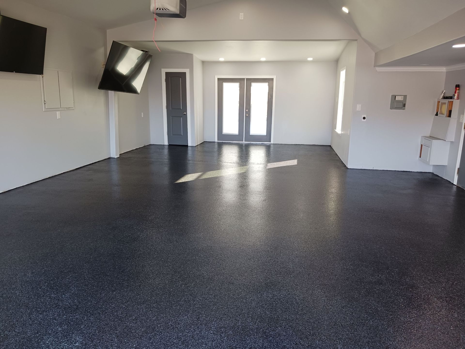 Garage with dark speckled epoxy floor, gray walls, and a doorway to the outside.