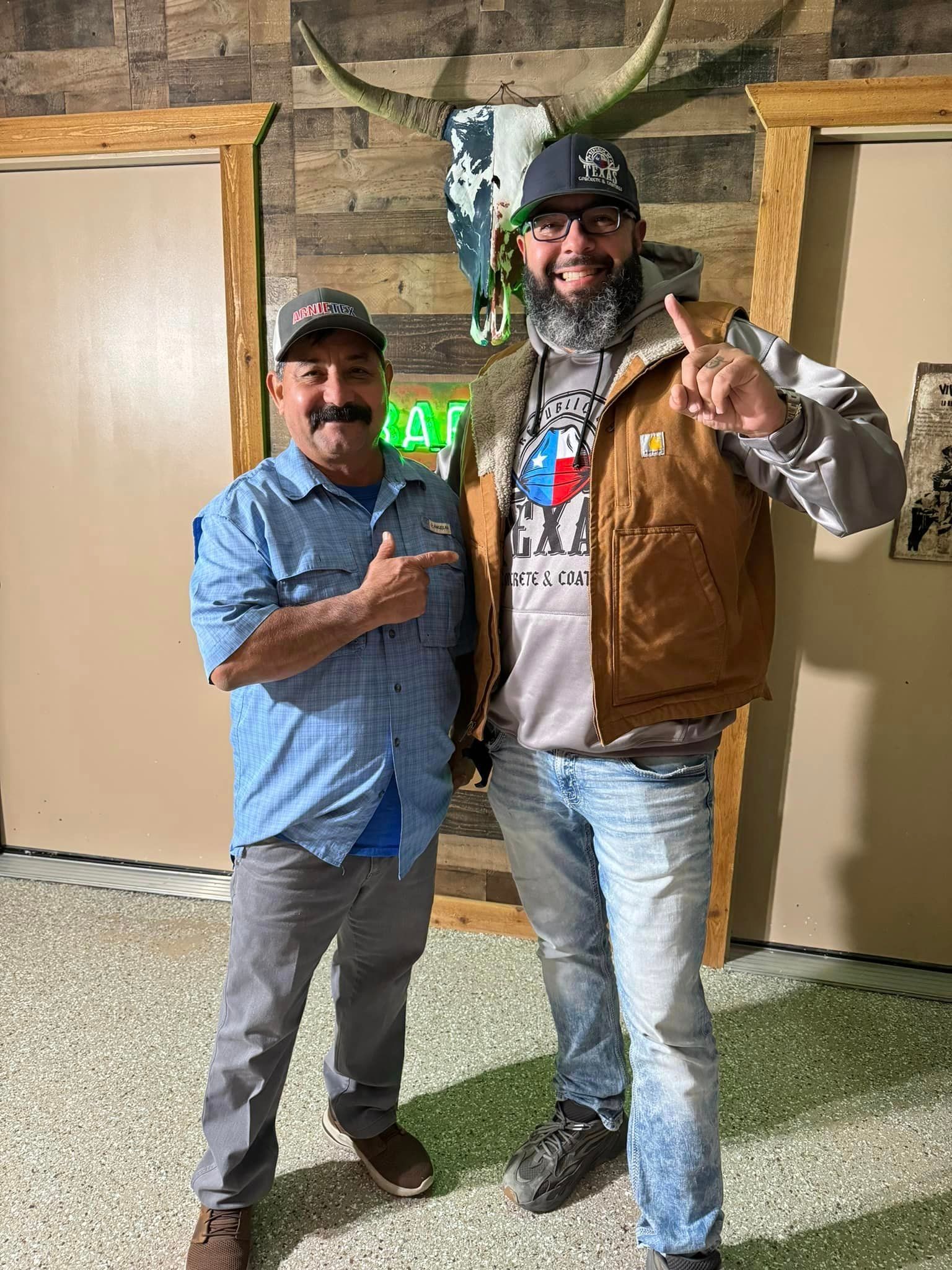 Two men standing near a mounted skull. One points, the other holds up a finger. Rustic interior.