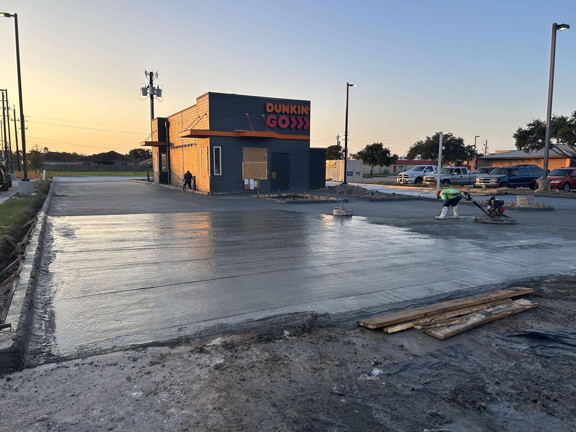 Construction of a Dunkin' location; fresh concrete being smoothed; worker in safety vest.