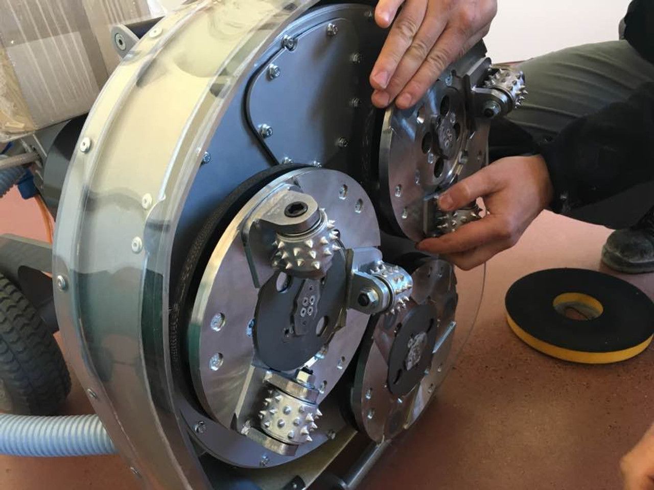 Person assembling a floor grinder machine, showing the grinding plates and gears.