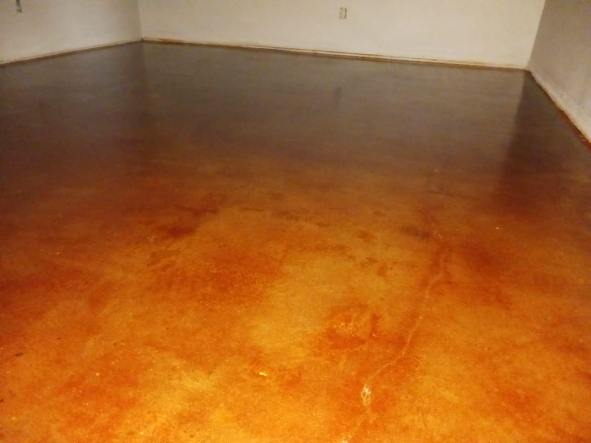 Polished concrete floor in shades of orange and brown, reflecting light in an empty room.