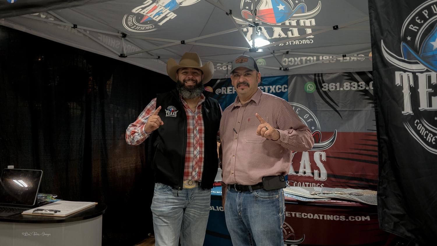 Two men in cowboy hats posing at a booth with Texas logos; one gives a thumbs up, one a fist.