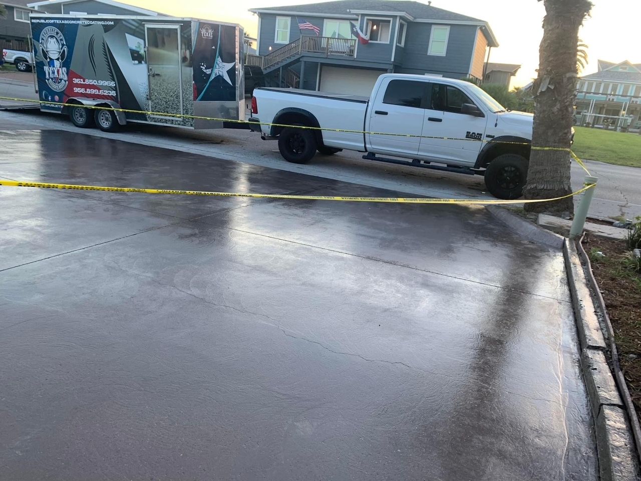 White truck towing a trailer on a freshly paved concrete driveway; yellow caution tape in foreground.
