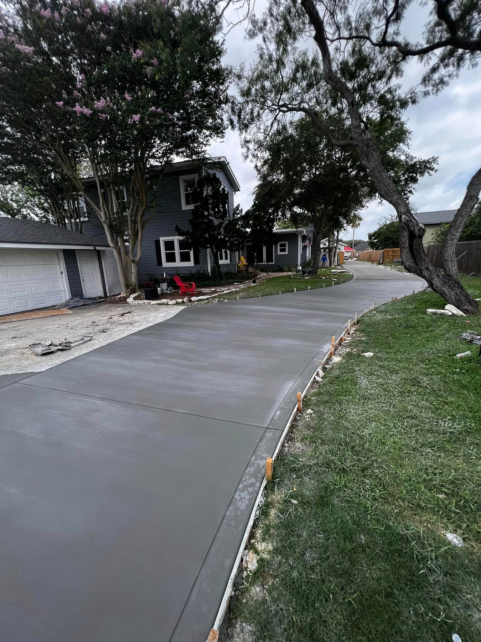 Newly poured concrete driveway in front of a gray house, bordered by grass and trees.