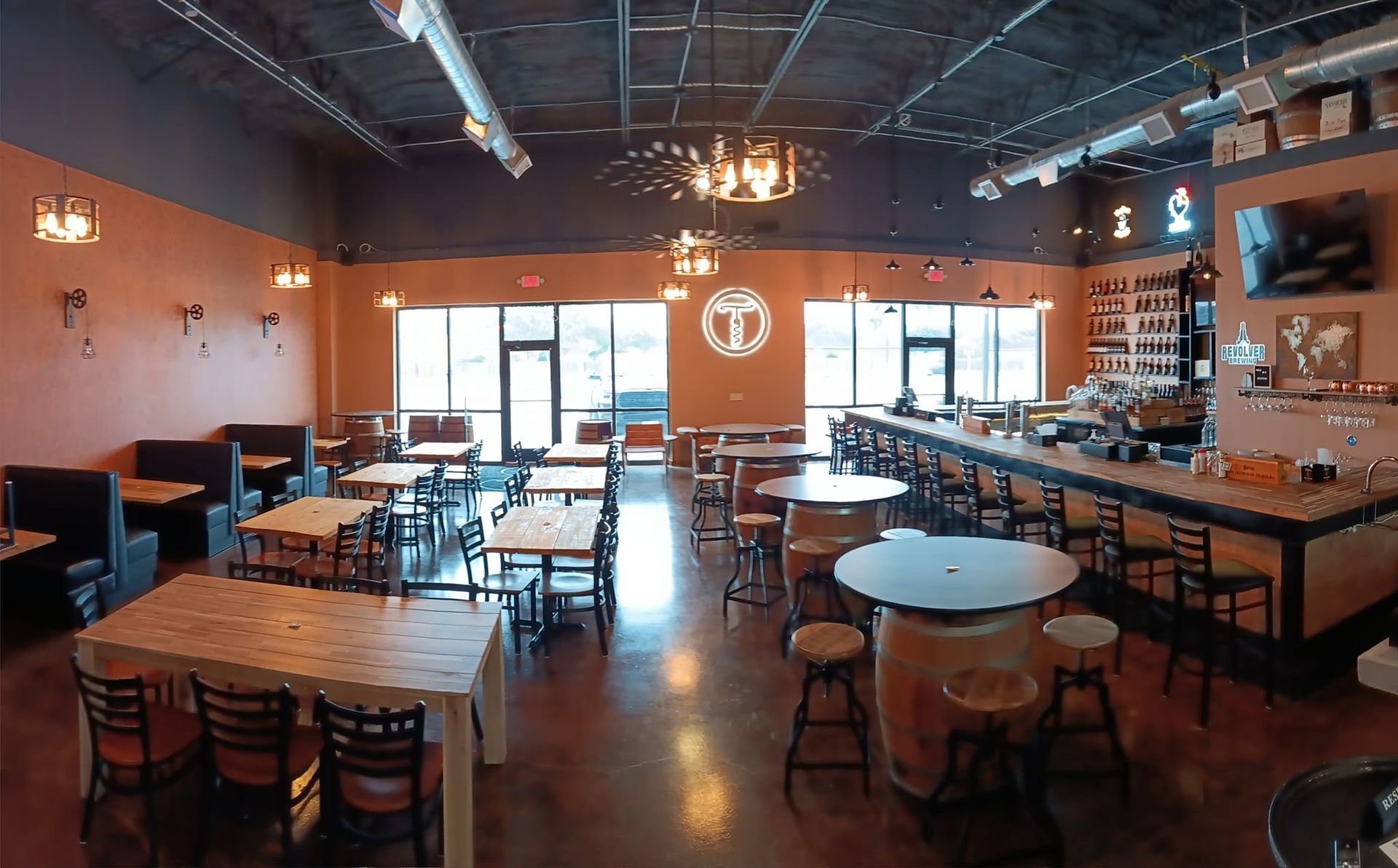 Interior view of a restaurant. Tables and booths are set up for dining. A bar and large windows are visible.