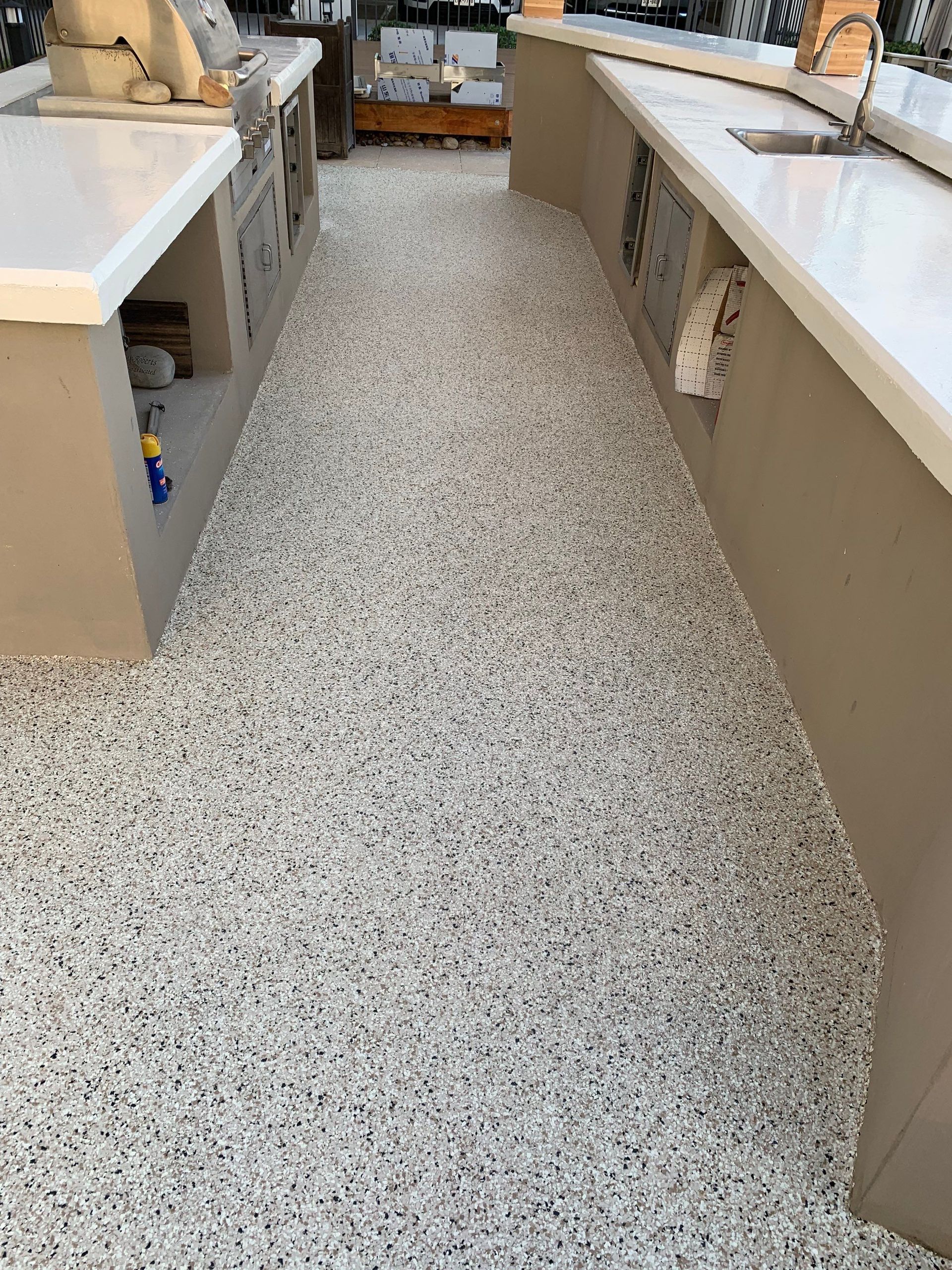 Outdoor kitchen with speckled flooring and light-colored countertops. Beige cabinets.