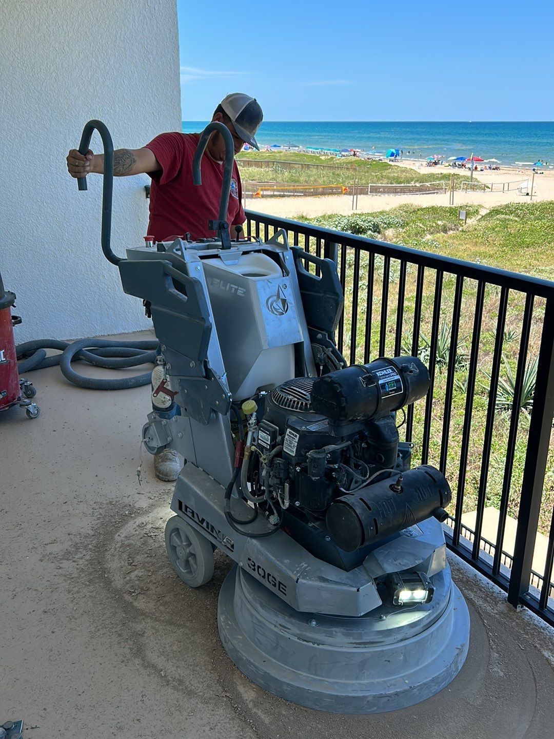 Man operating a concrete grinder on a balcony overlooking the beach.
