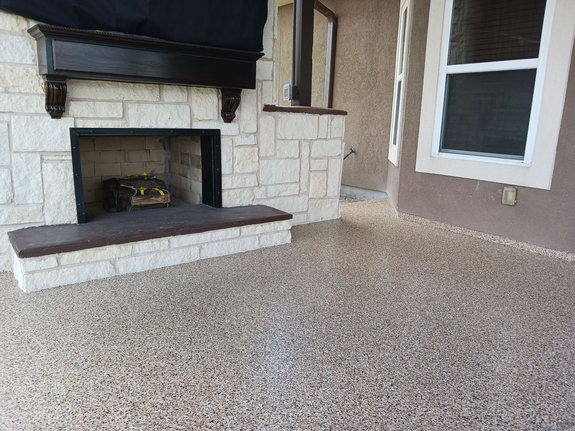 Stone fireplace on a speckled brown patio, next to a window on a tan wall.