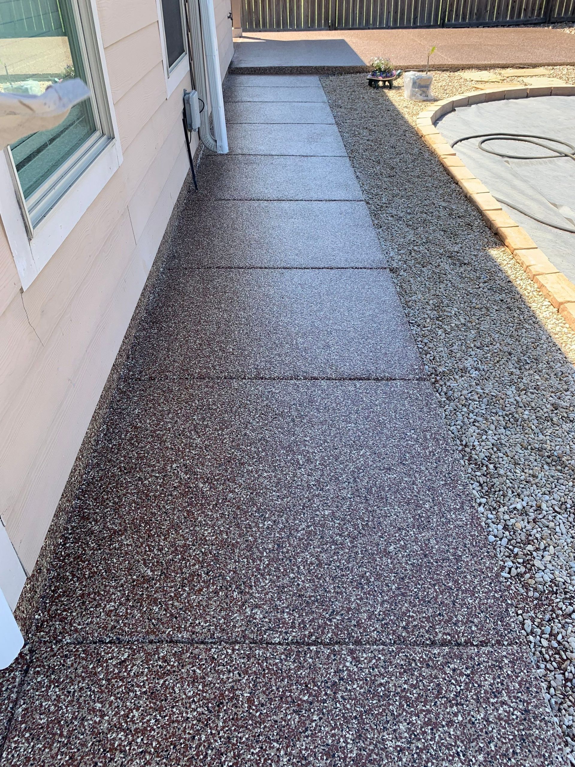 A textured, speckled concrete walkway next to a building, with a dark brown and gray color palette.