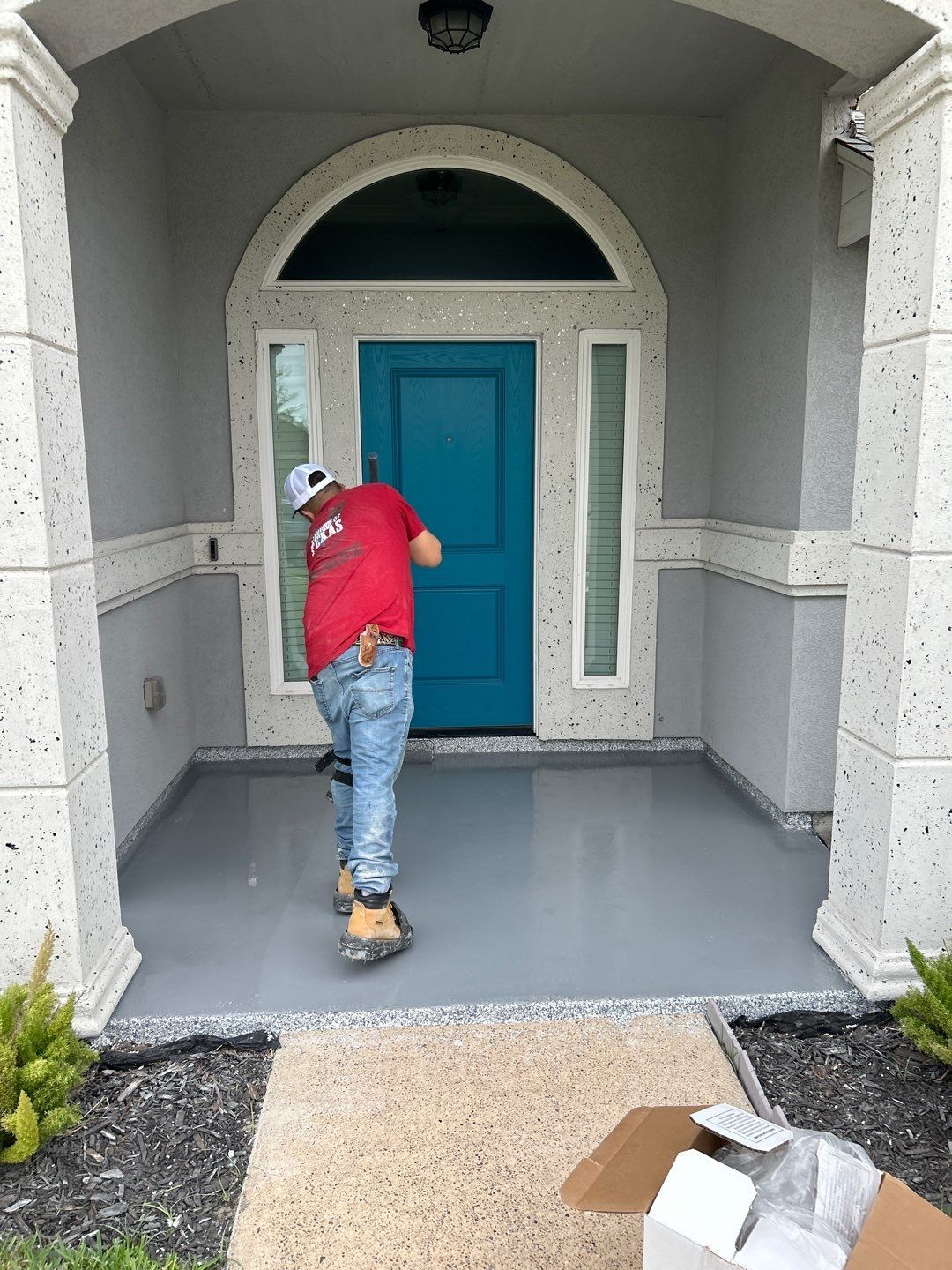 Person in red shirt on a gray-painted porch, teal door, beige trim, light gray exterior walls.
