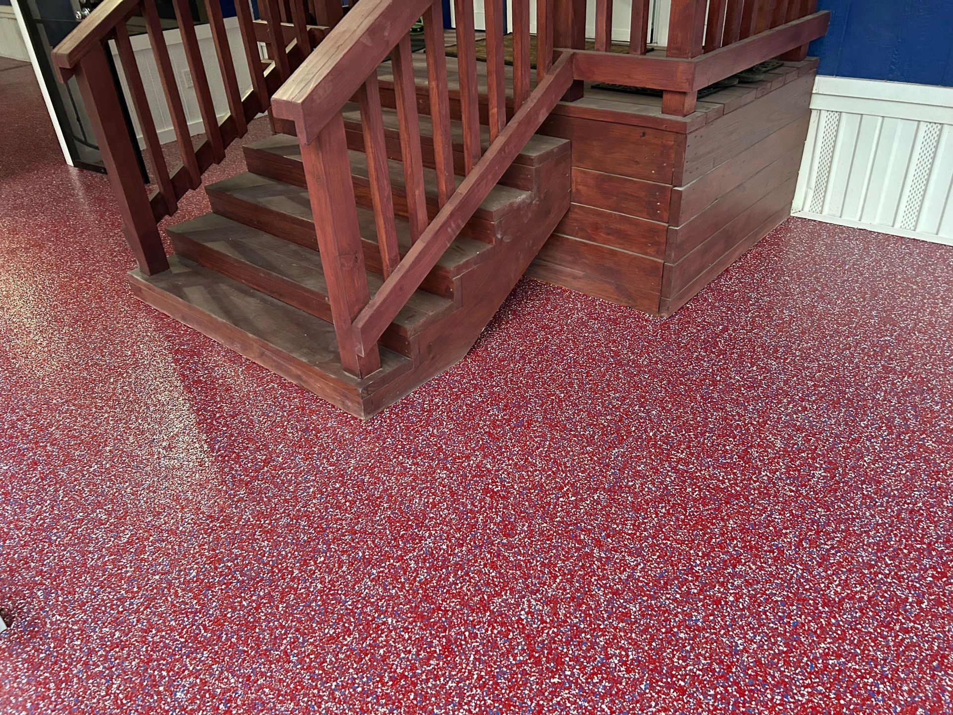 Staircase with wooden steps and railing on a red speckled floor.