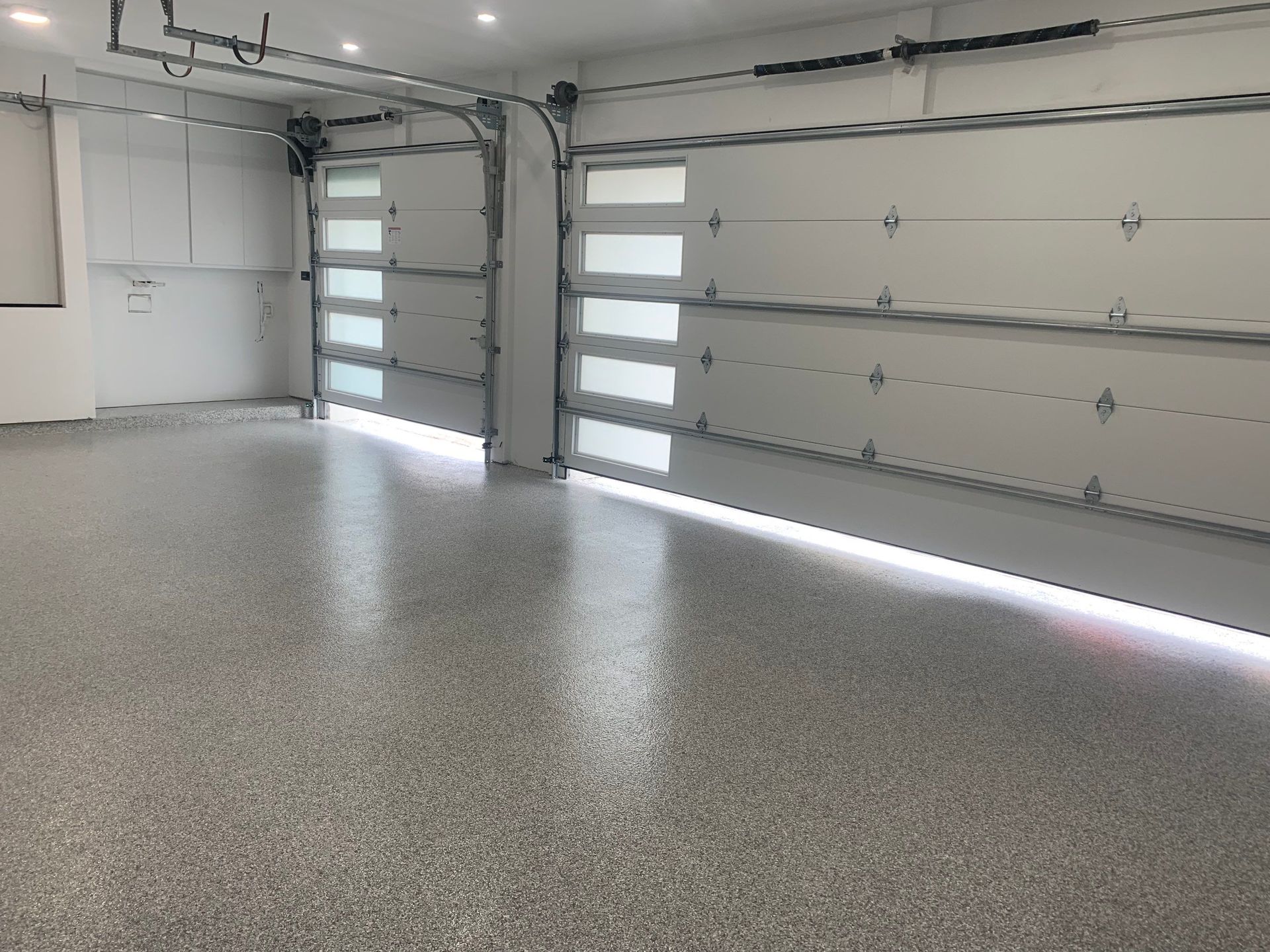 Garage interior with two white garage doors, epoxy floor, and overhead storage cabinets.