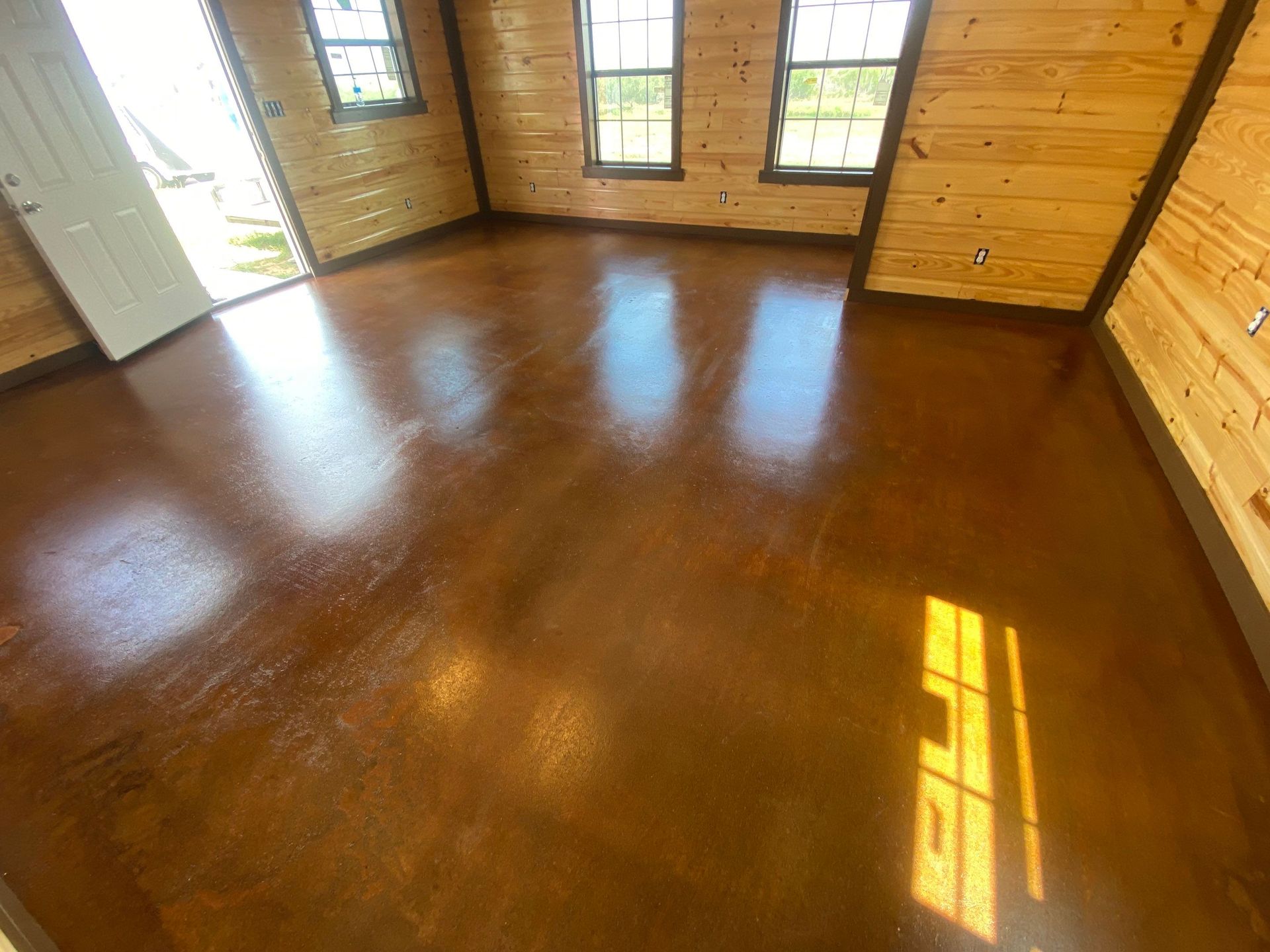 Room with polished, brown floor and wood-paneled walls. Sunlight streams through windows.