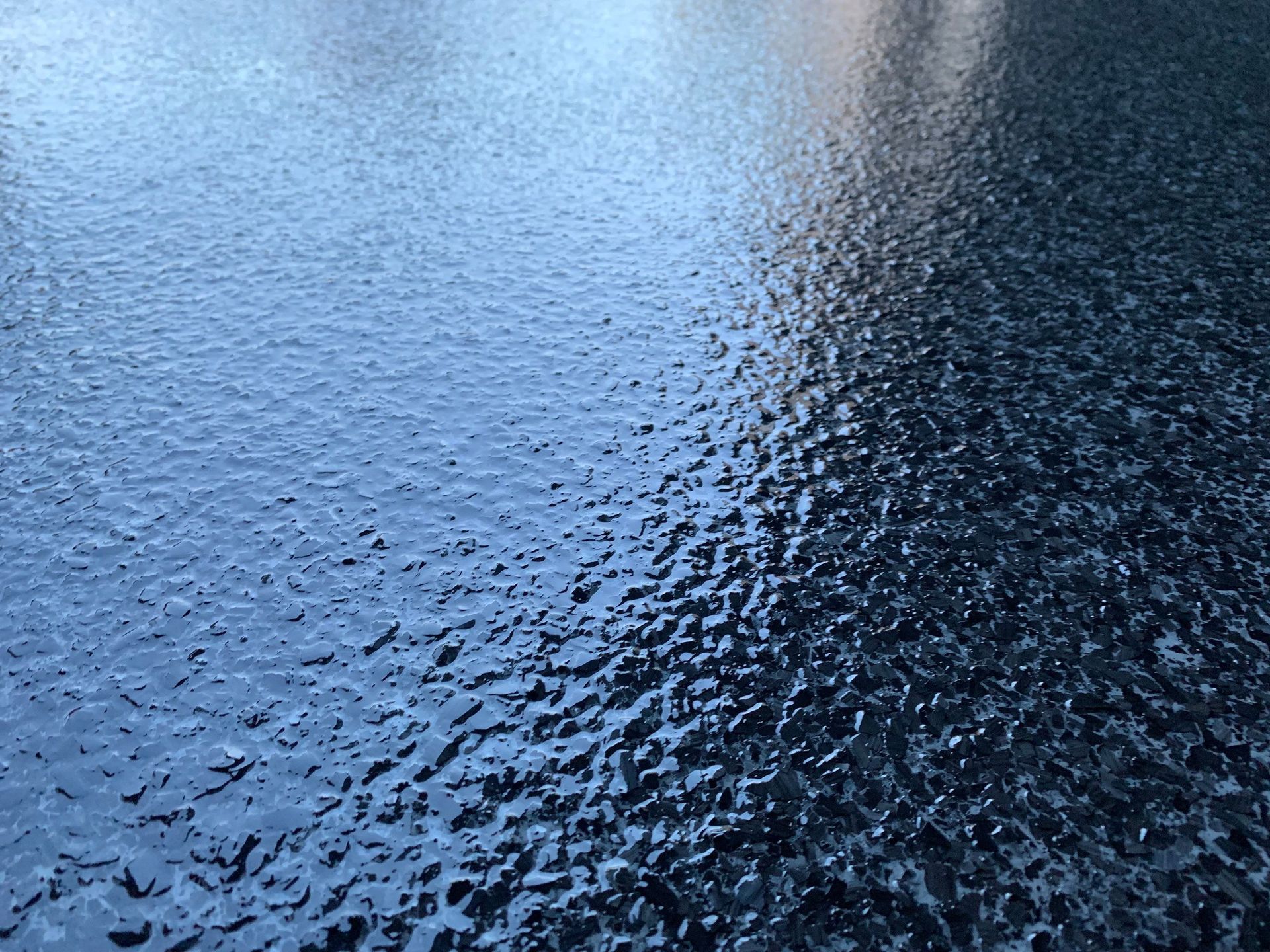 Glazed ice on a dark surface, reflecting light.