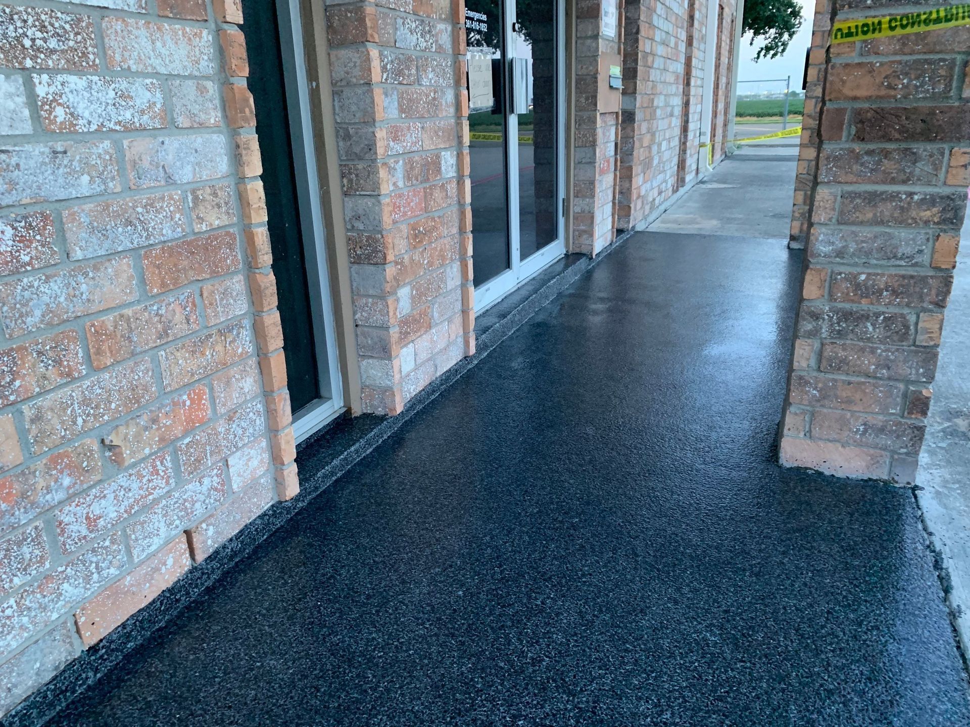Dark epoxy-coated concrete walkway outside a brick building. Black and gray speckles on the ground.
