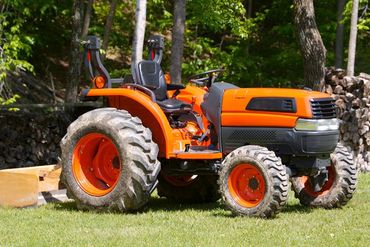 a small orange tractor is parked in a grassy field .
