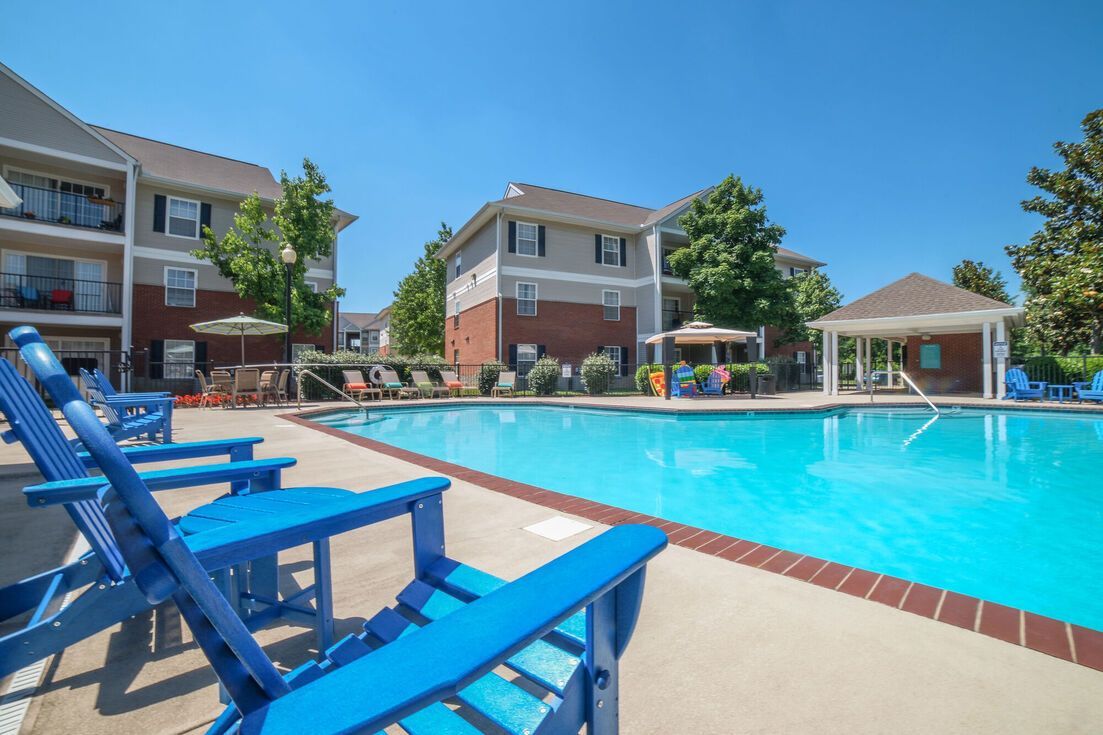 Poolside scene with blue chairs, pool, and apartment buildings under a blue sky.